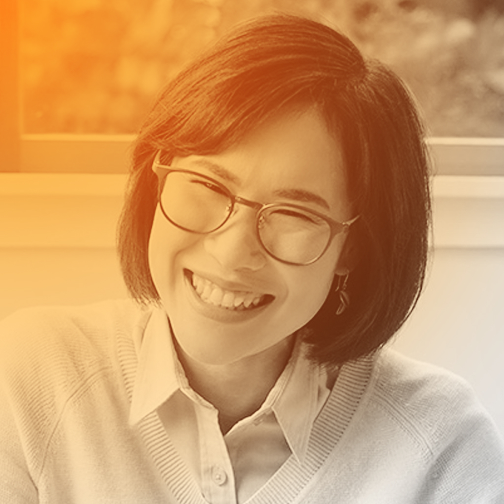 Prae's portrait. A laughing Thai woman with short dark hair and a large pair of dark rimmed glasses.