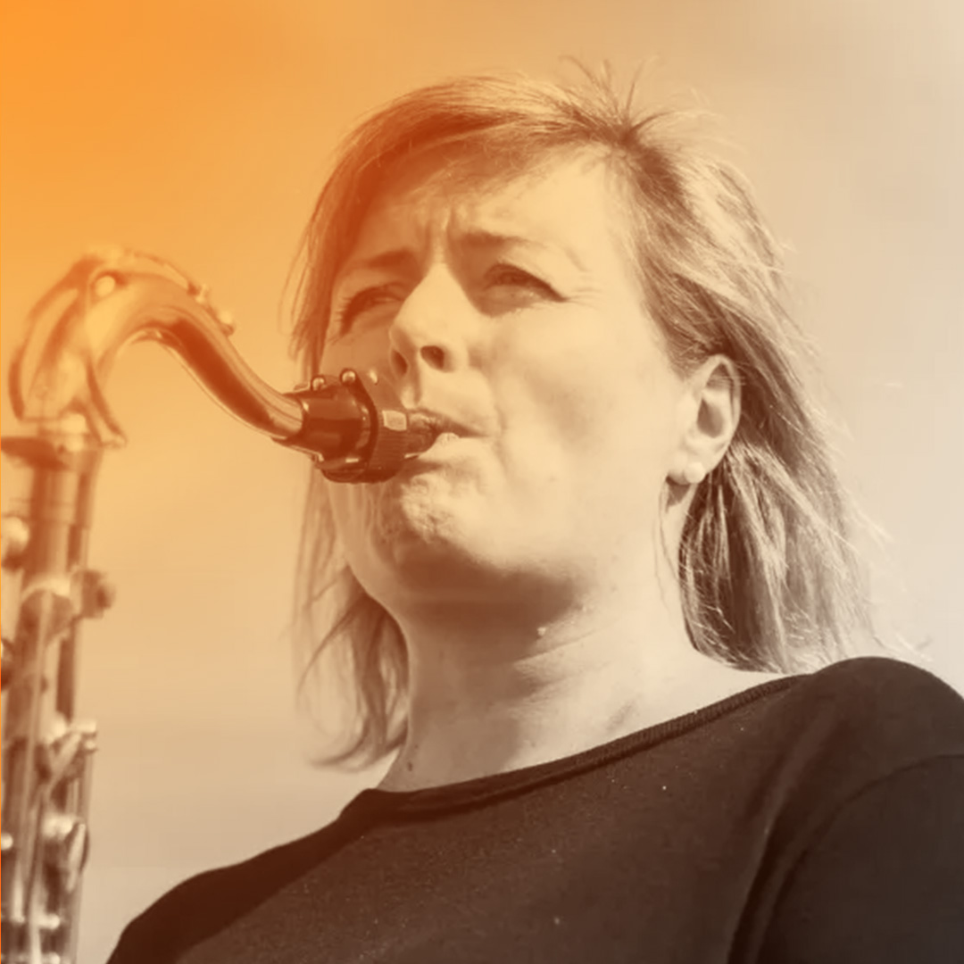 Straight-haired, blue-eyed, freckly middle-aged Pakeha woman playing the saxophone.